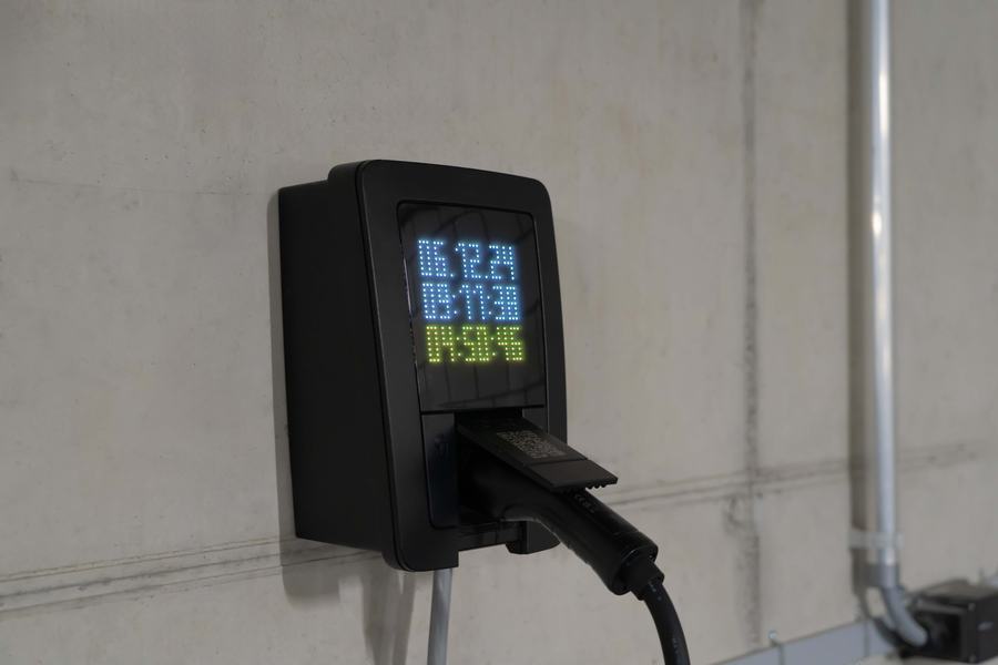 Borne de recharge noire à écran numérique fixée sur un mur de béton, avec un connecteur branché