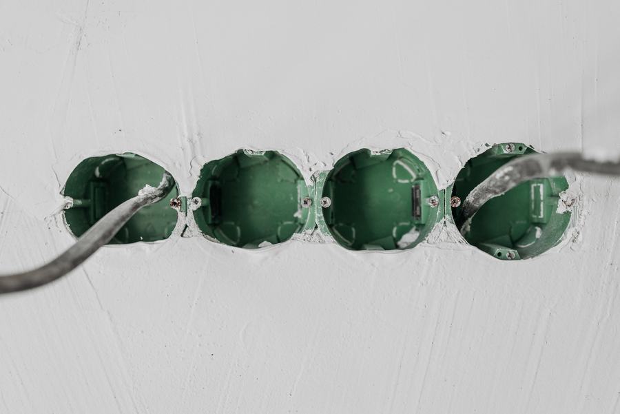 Quatre boîtiers d'encastrement verts alignés dans un mur blanc, avec les câbles qui en sortent